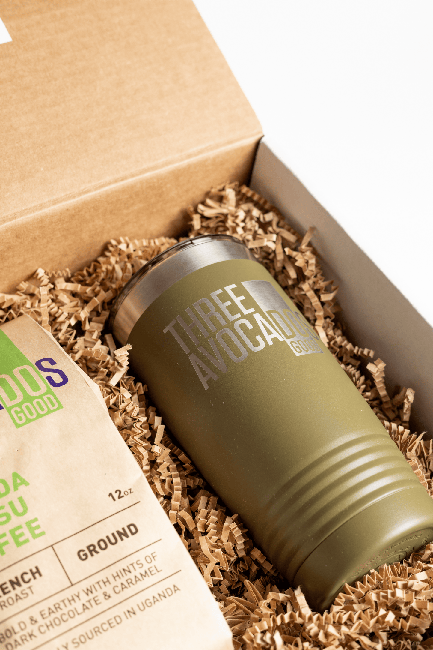 A tumbler and bag of coffee in a box, lid open, focused on the tumbler