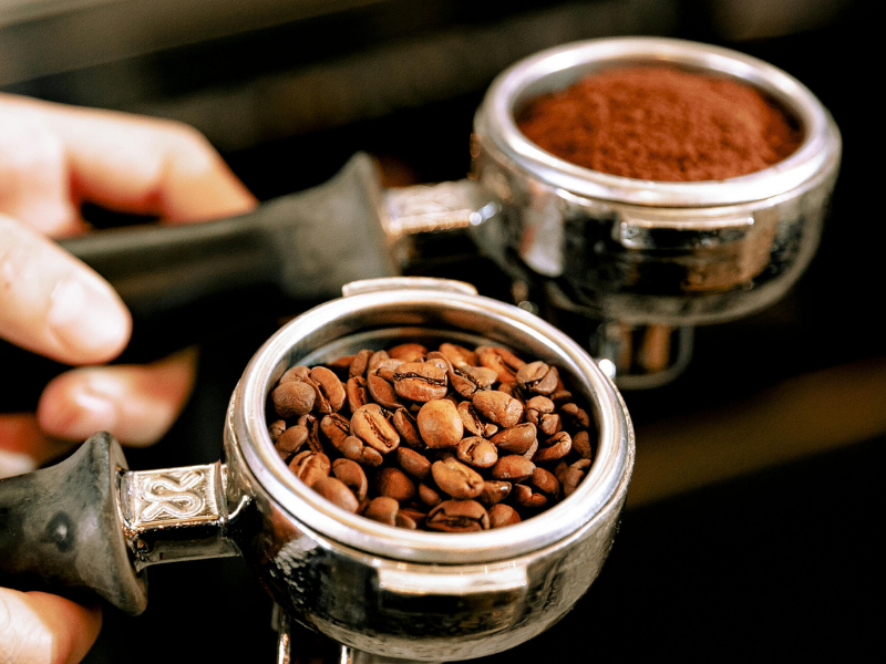 An image of coffee beans and coffee grounds in two espresso machine holders