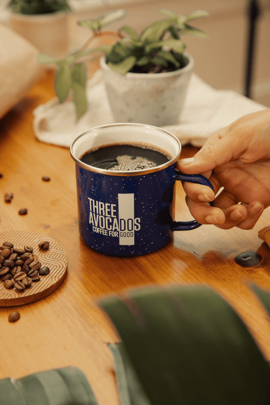 A hand holding a blue enamel mug of coffee