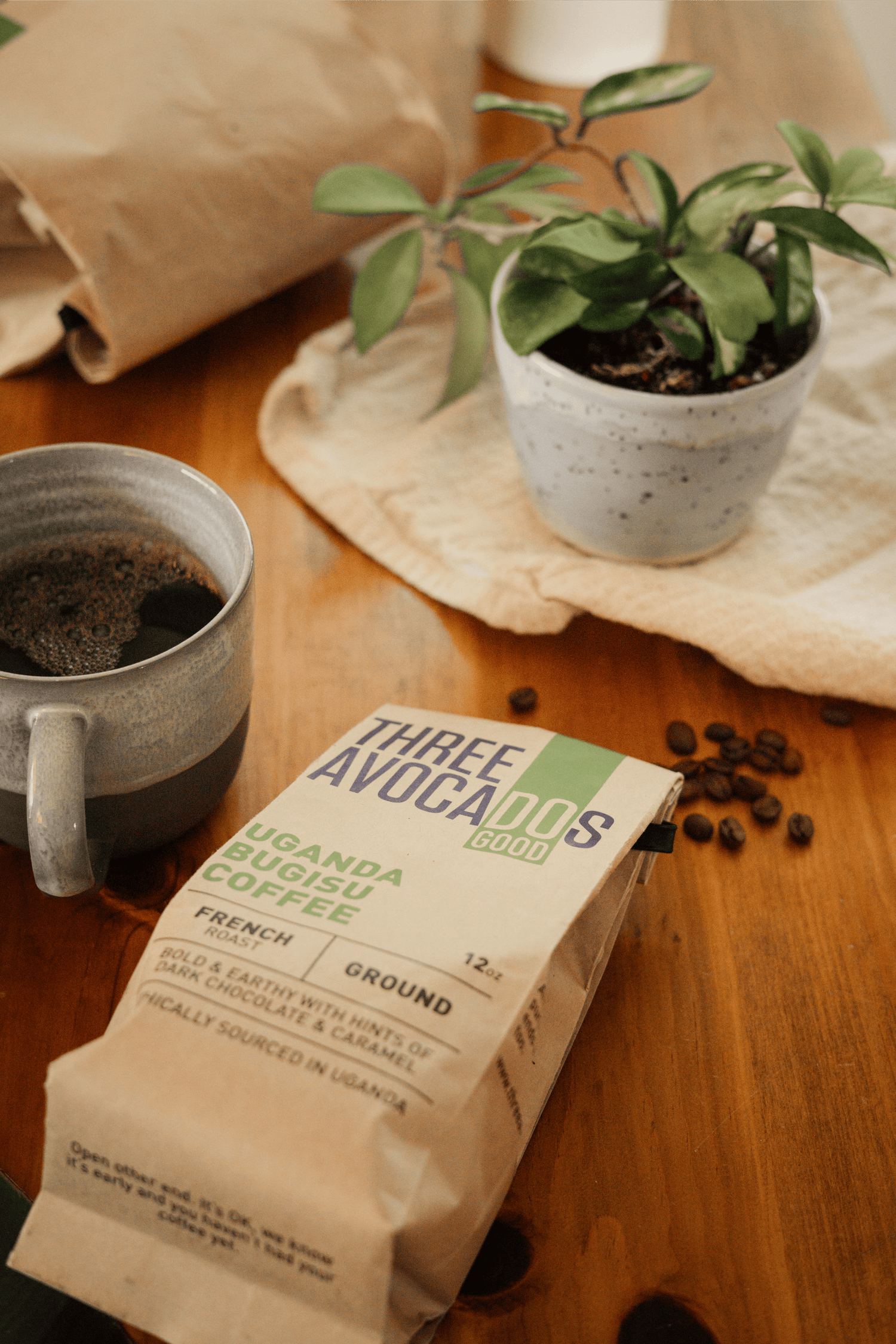 Mug, plant, and coffee bag with overflowing beans all lying on a wood table