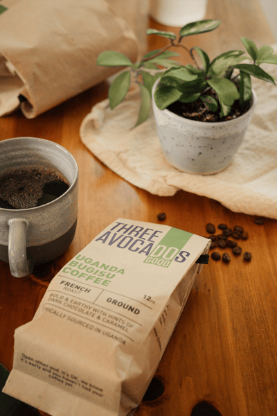 Mug, plant, and coffee bag with overflowing beans all lying on a wood table